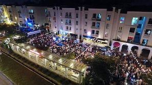 Gran reunión al aire libre frente a un edificio con varios balcones y un corredor cubierto.