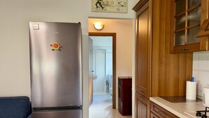 Une cuisine équipée d’un réfrigérateur en acier inoxydable, de meubles de rangement en bois, d’un évier et d’un plan de travail sur lequel se trouve une bouilloire.