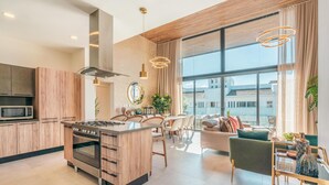 Een moderne keuken met een centraal eiland, een eetgedeelte met stoelen en een stadszicht door grote ramen.