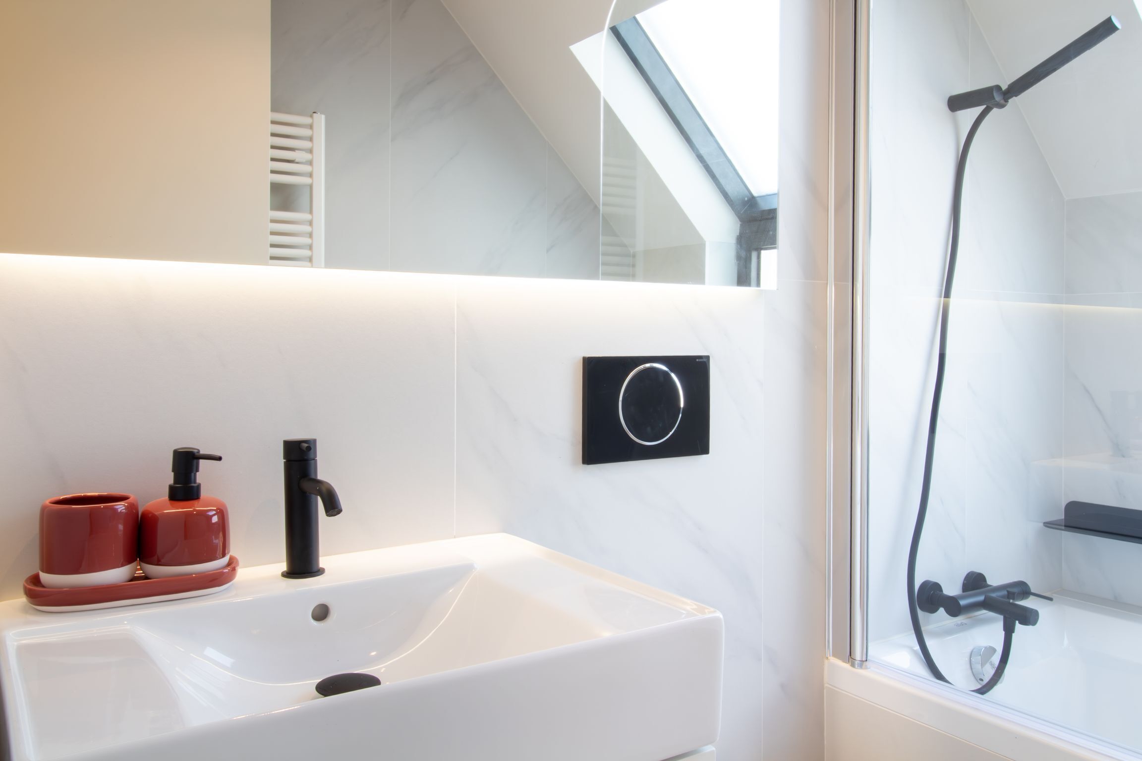 A modern bathroom with a white sink, black faucet, and red soap dispensers.
