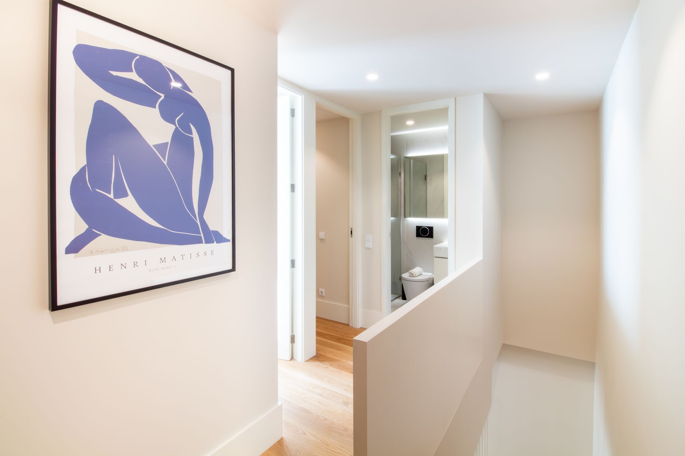 Un couloir orné d’une œuvre d’art abstraite encadrée au mur, qui mène à une salle de bain équipée d’un miroir et de toilettes.