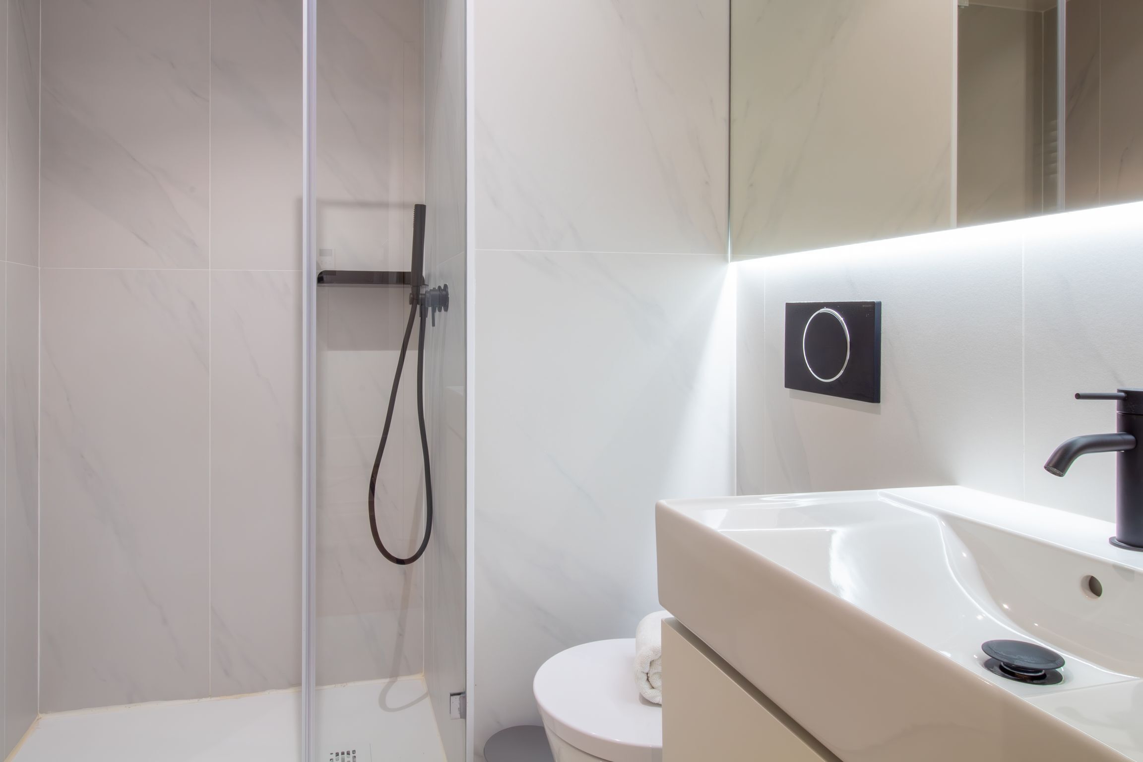Une salle de bain moderne avec une douche à parois de verre, des toilettes blanches et un lavabo doté d’un robinet noir.