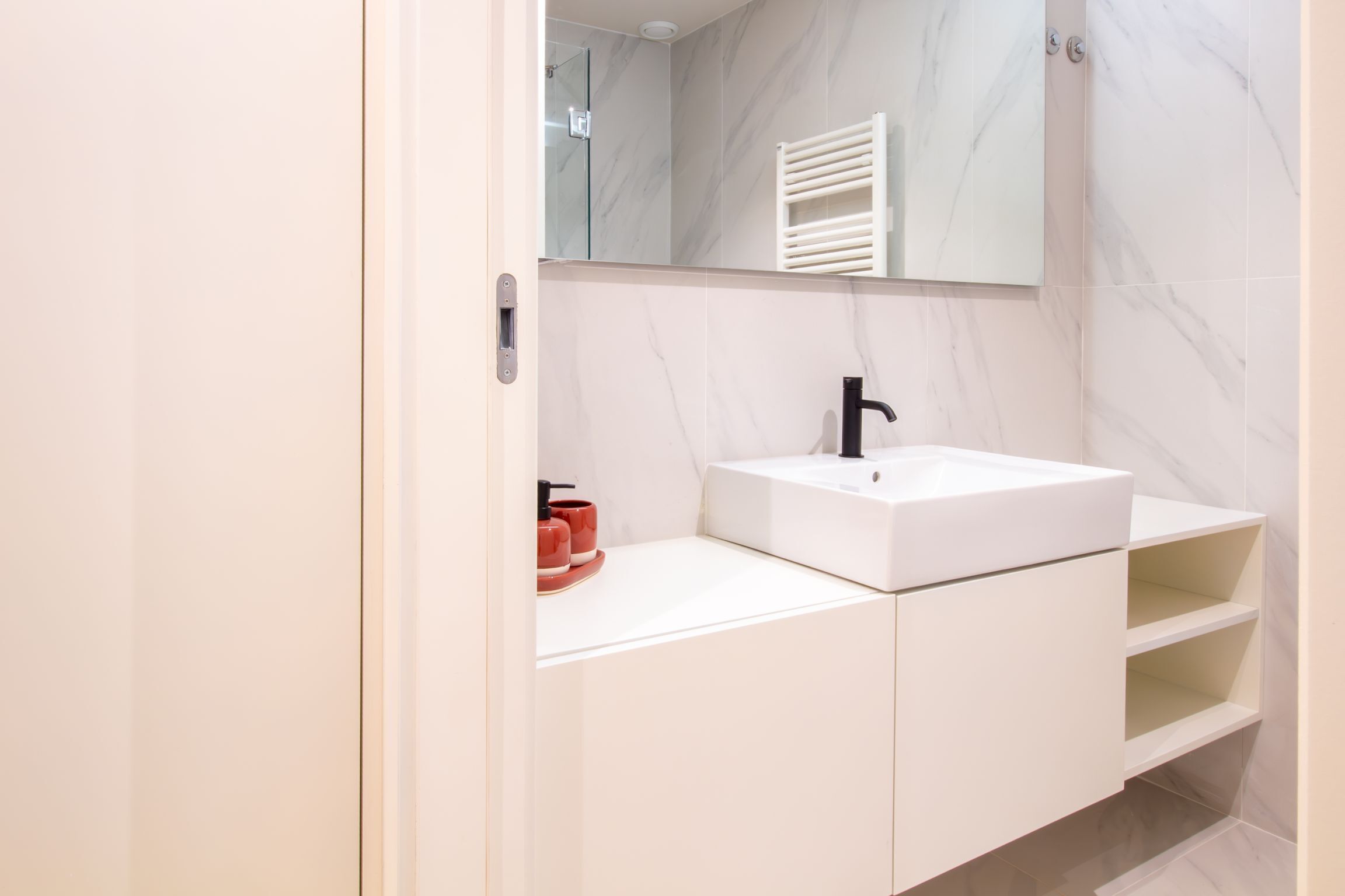 A modern bathroom with a white sink, black faucet, and a glass shower enclosure.