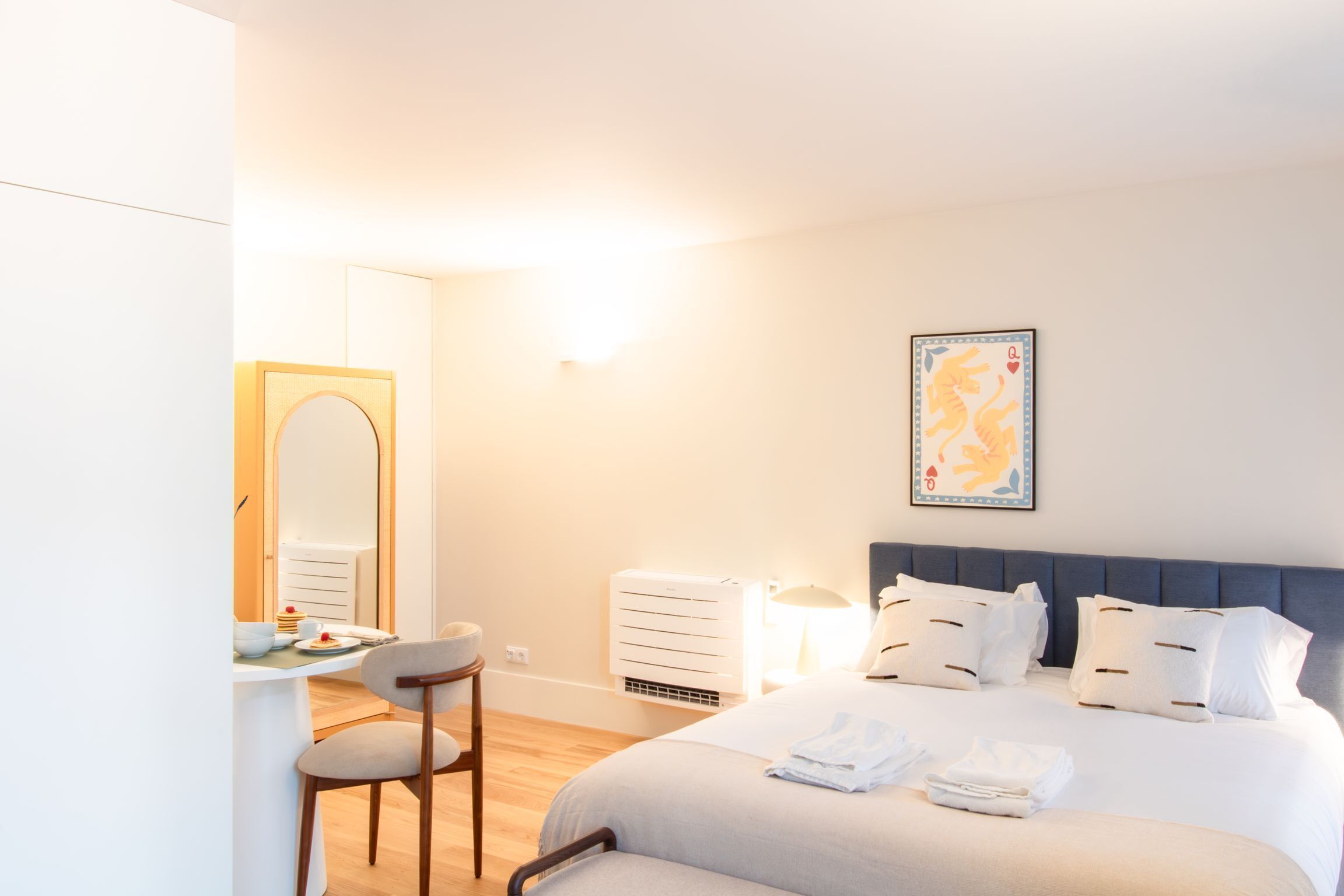 A hotel room with a bed, bedside table, chair, and a wall-mounted air conditioner.