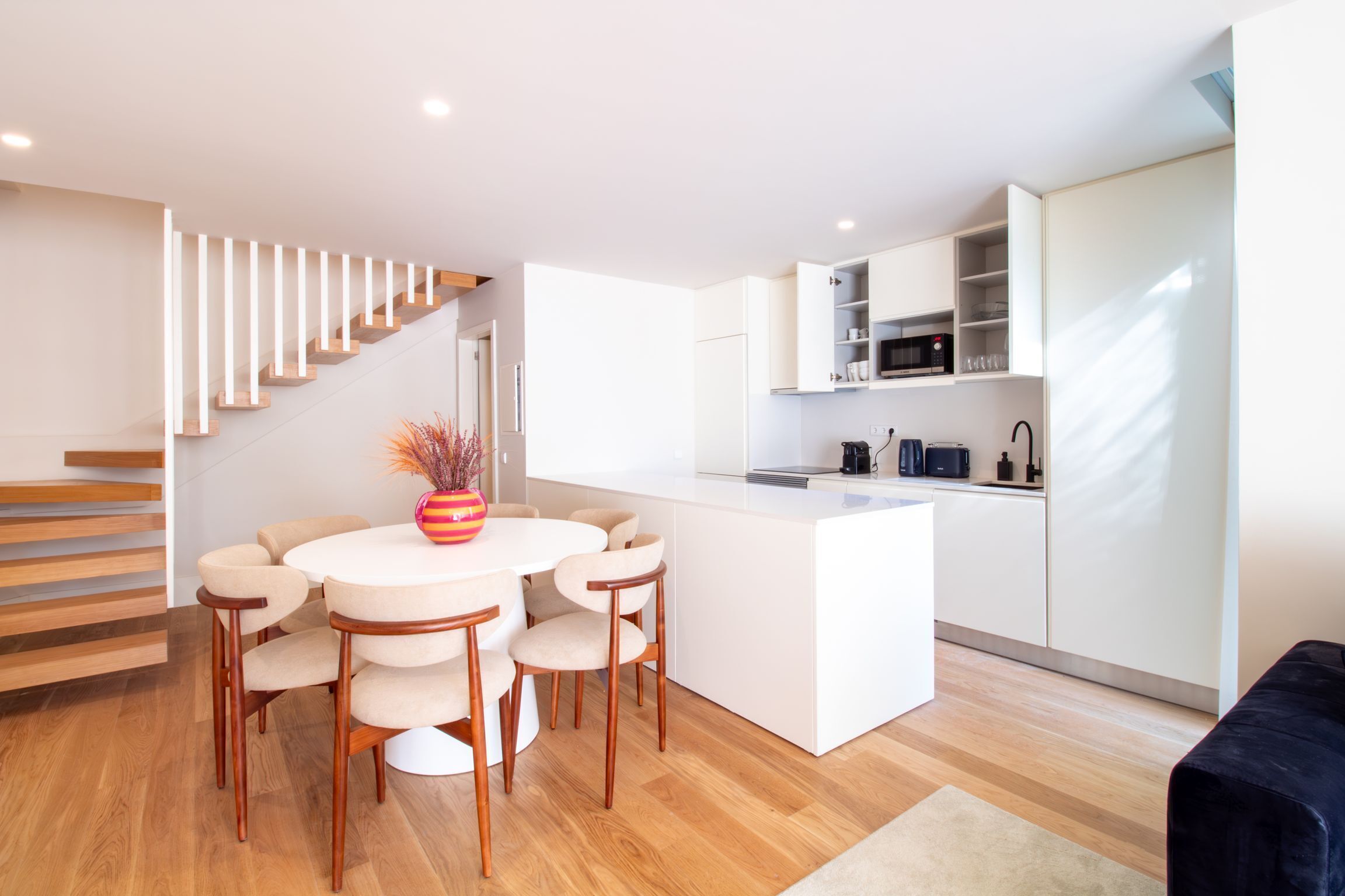 A modern kitchen with white cabinetry, a central island, and a dining area with a round table and chairs.