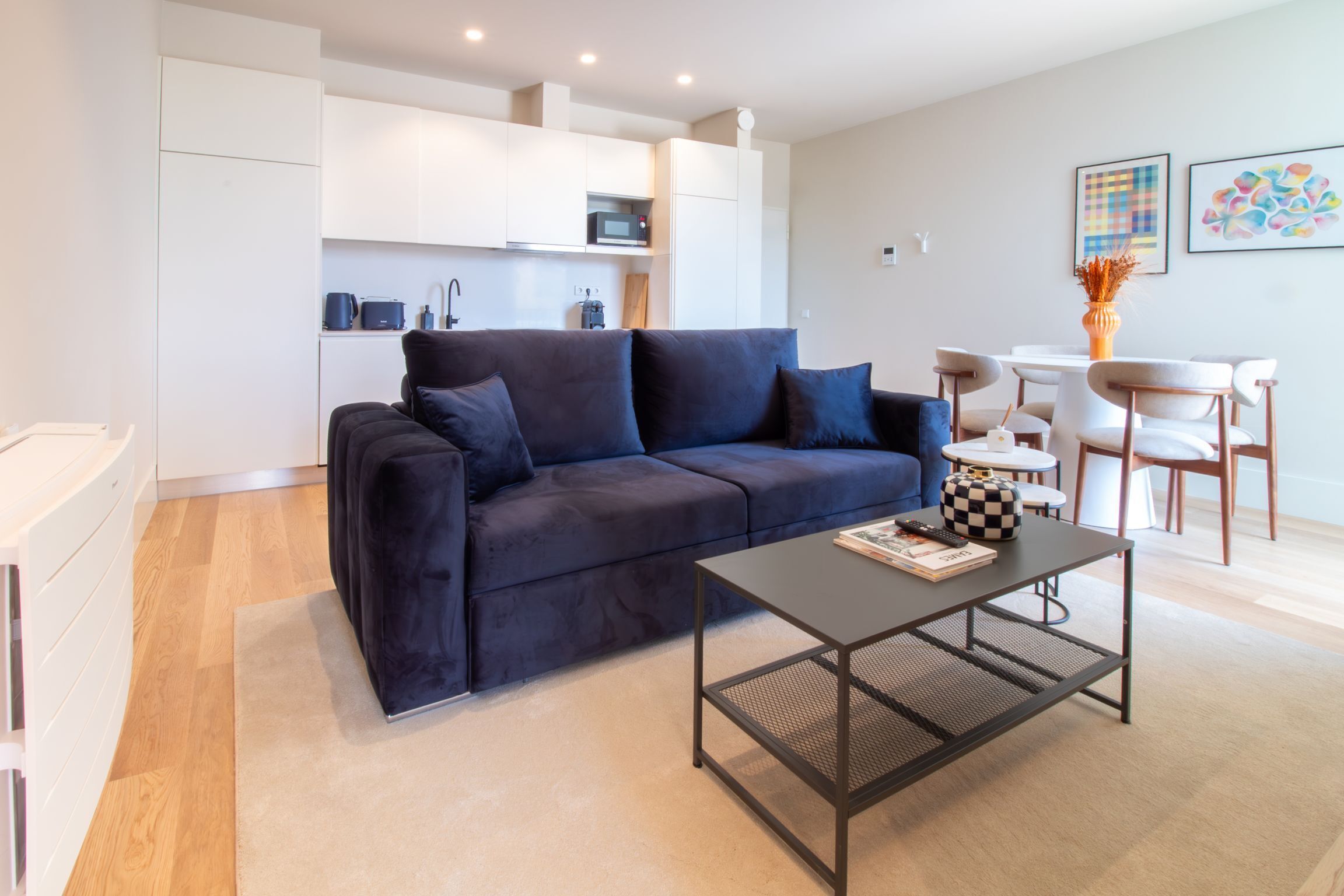 A modern living room with a dark blue sofa, a small coffee table, and a kitchen area in the background.
