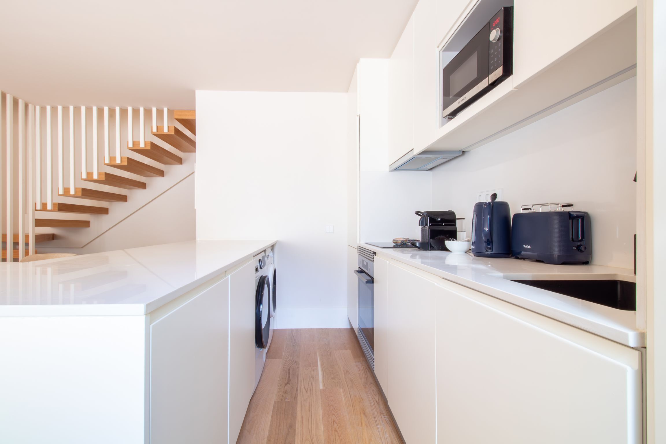 A modern kitchen with white cabinetry, a built-in washing machine, a microwave, and a toaster.
