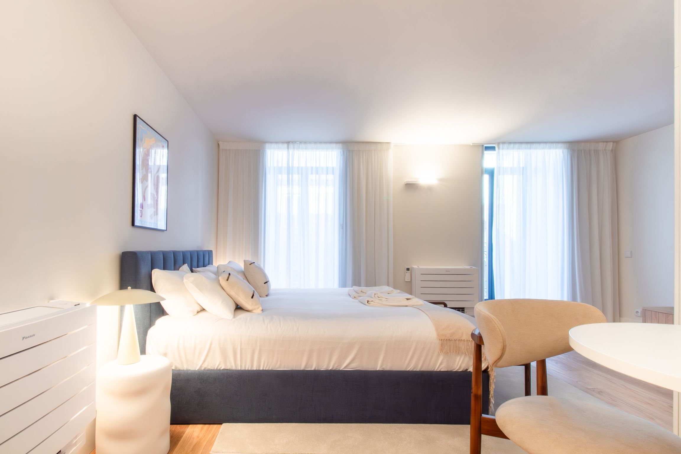 Un dormitorio moderno con cama, mesita de noche, lámpara y una silla.