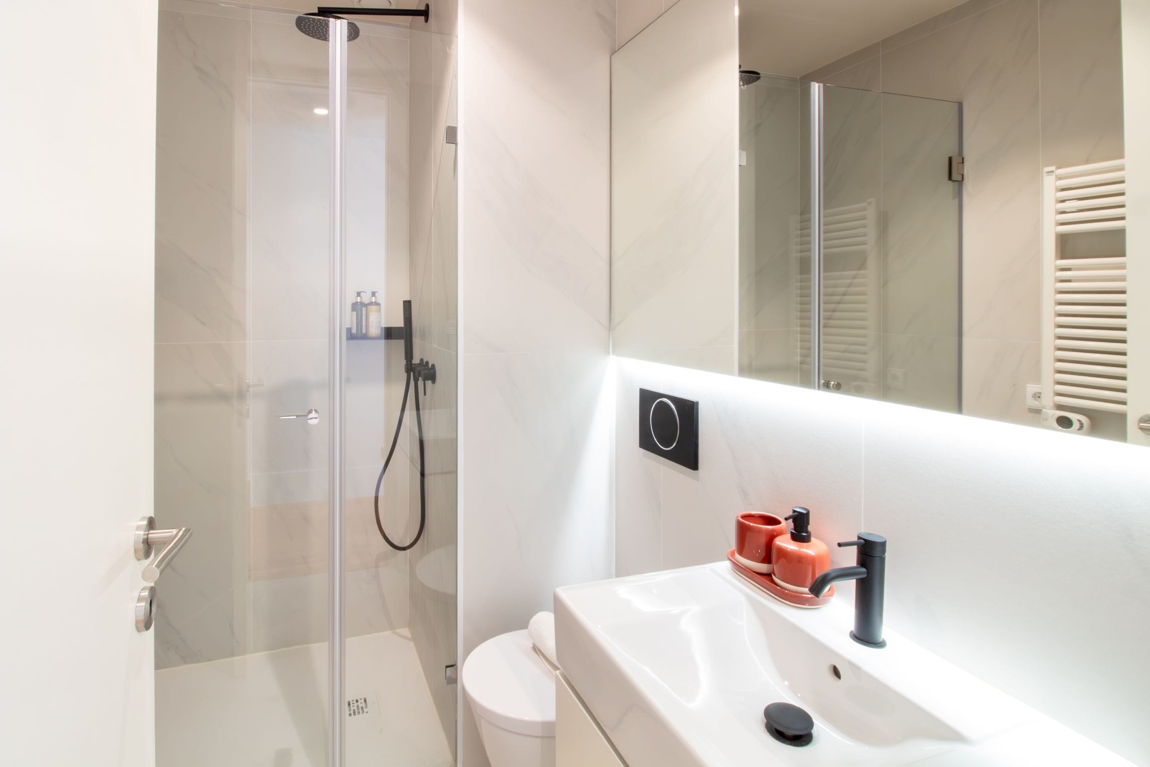 A modern bathroom with a glass-enclosed shower, a white sink, and a large mirror.