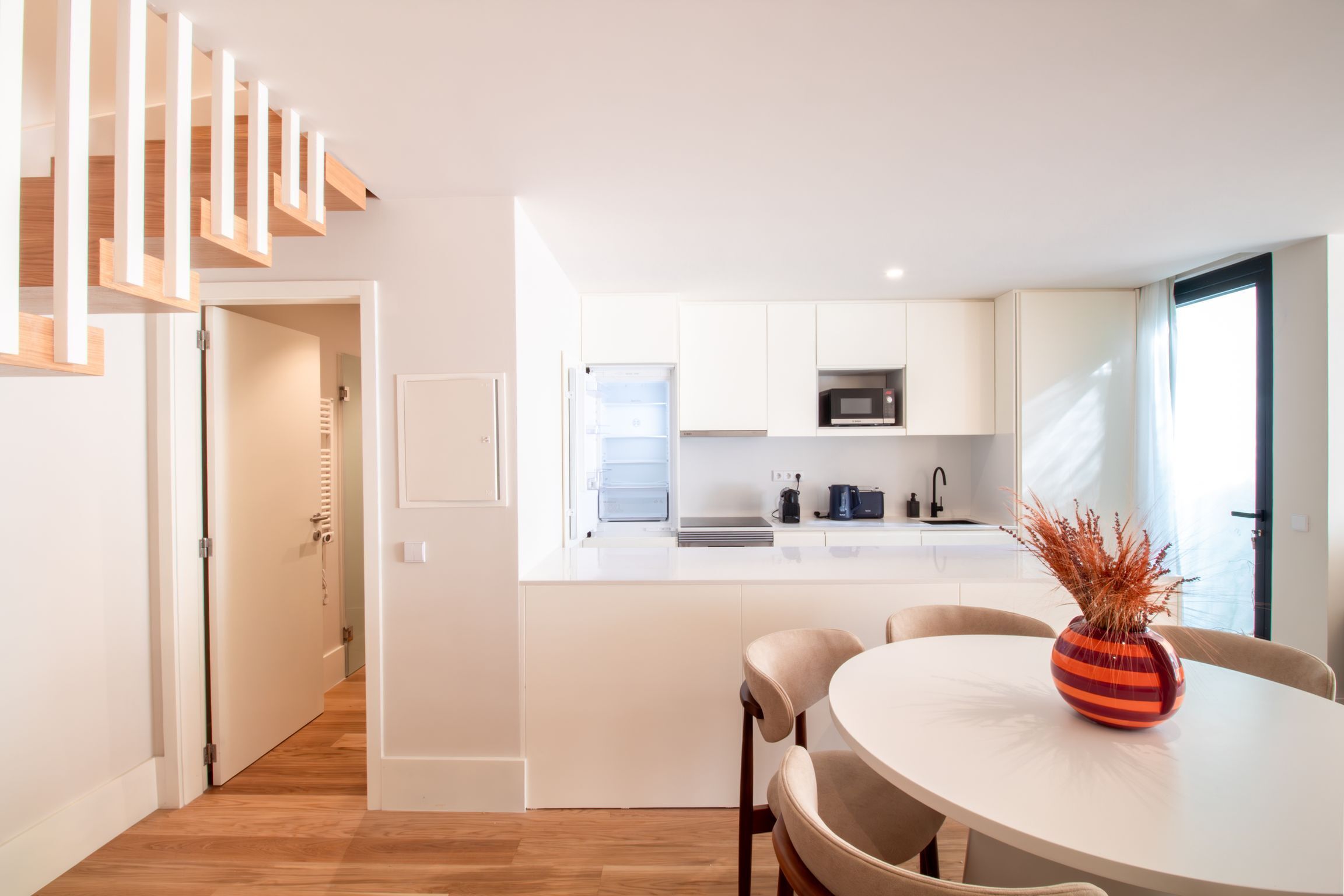 A modern kitchen with white cabinets, a microwave, and a dining area with a round table and chairs.