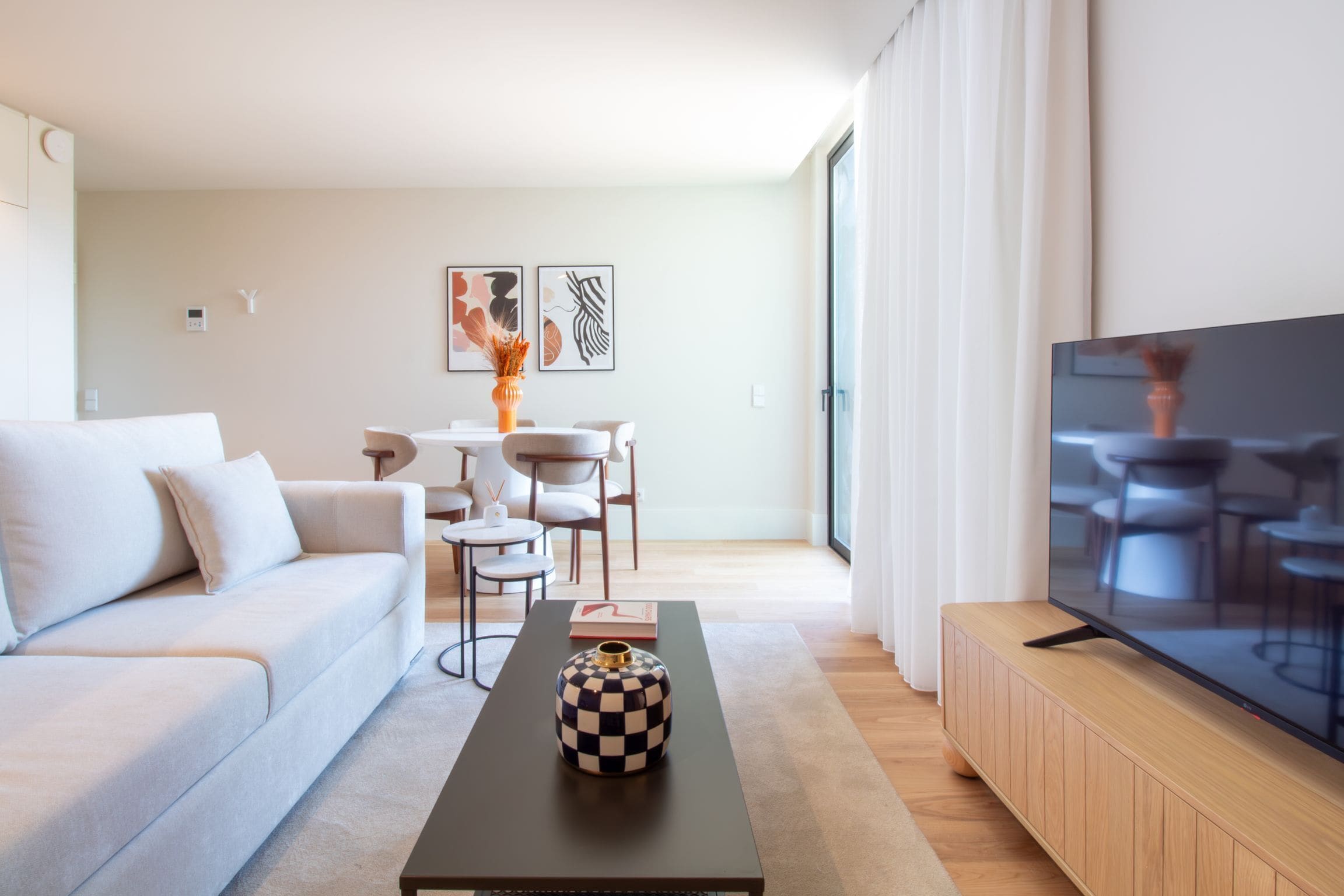 A modern living room with a sofa, a coffee table with a decorative vase, a dining area with chairs and a table, and a TV on a wooden stand.