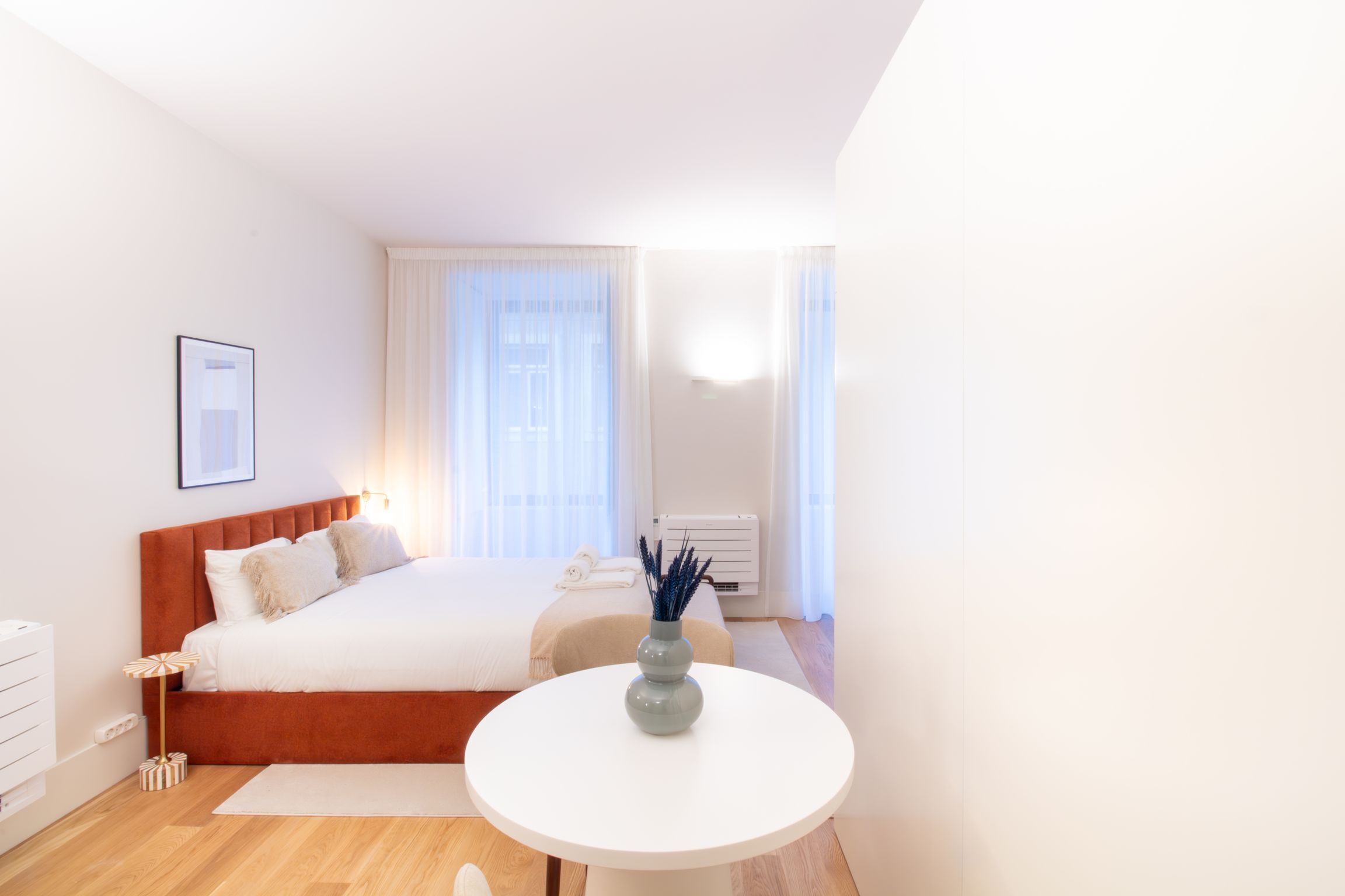 A modern hotel room with a large bed, a round white table, and a vase of blue flowers.