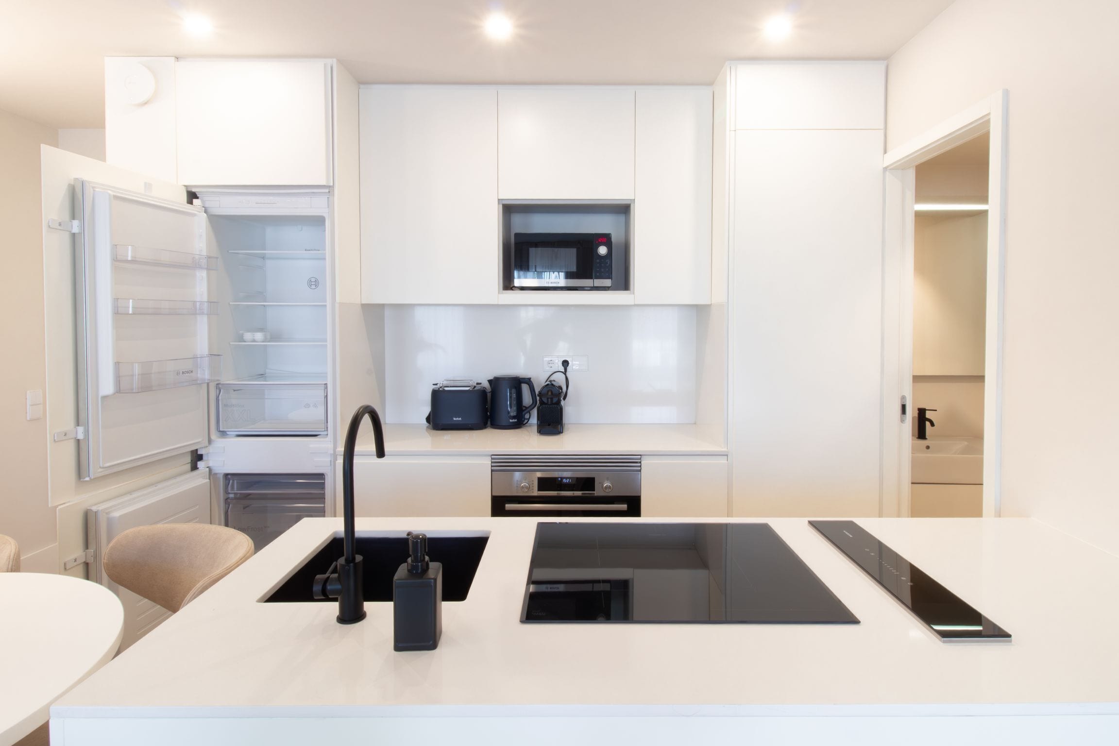 A modern kitchen with white cabinetry, a built-in microwave, a coffee maker, and a black induction cooktop.