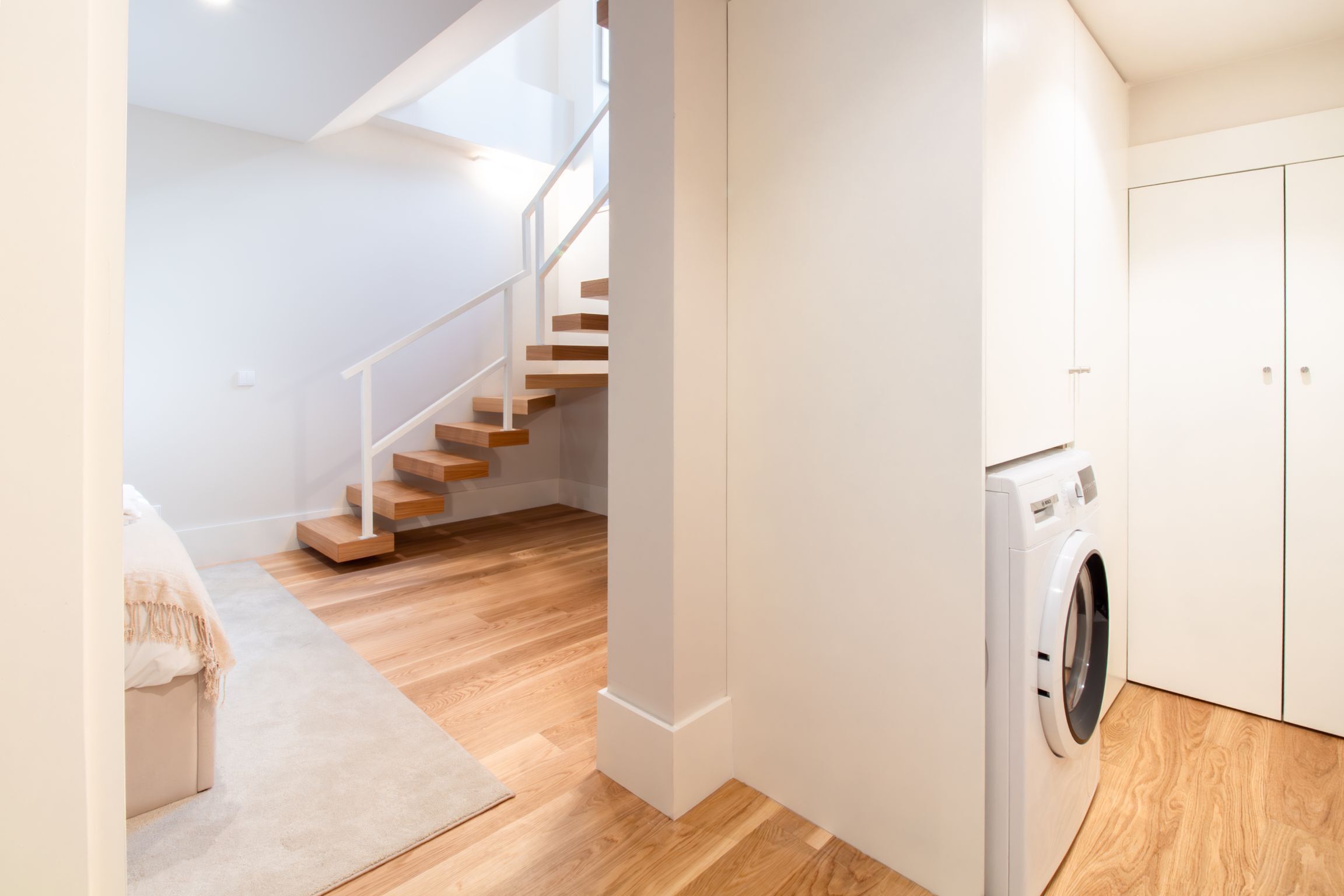 A modern apartment with a wooden staircase, a washing machine, and a beige sofa.