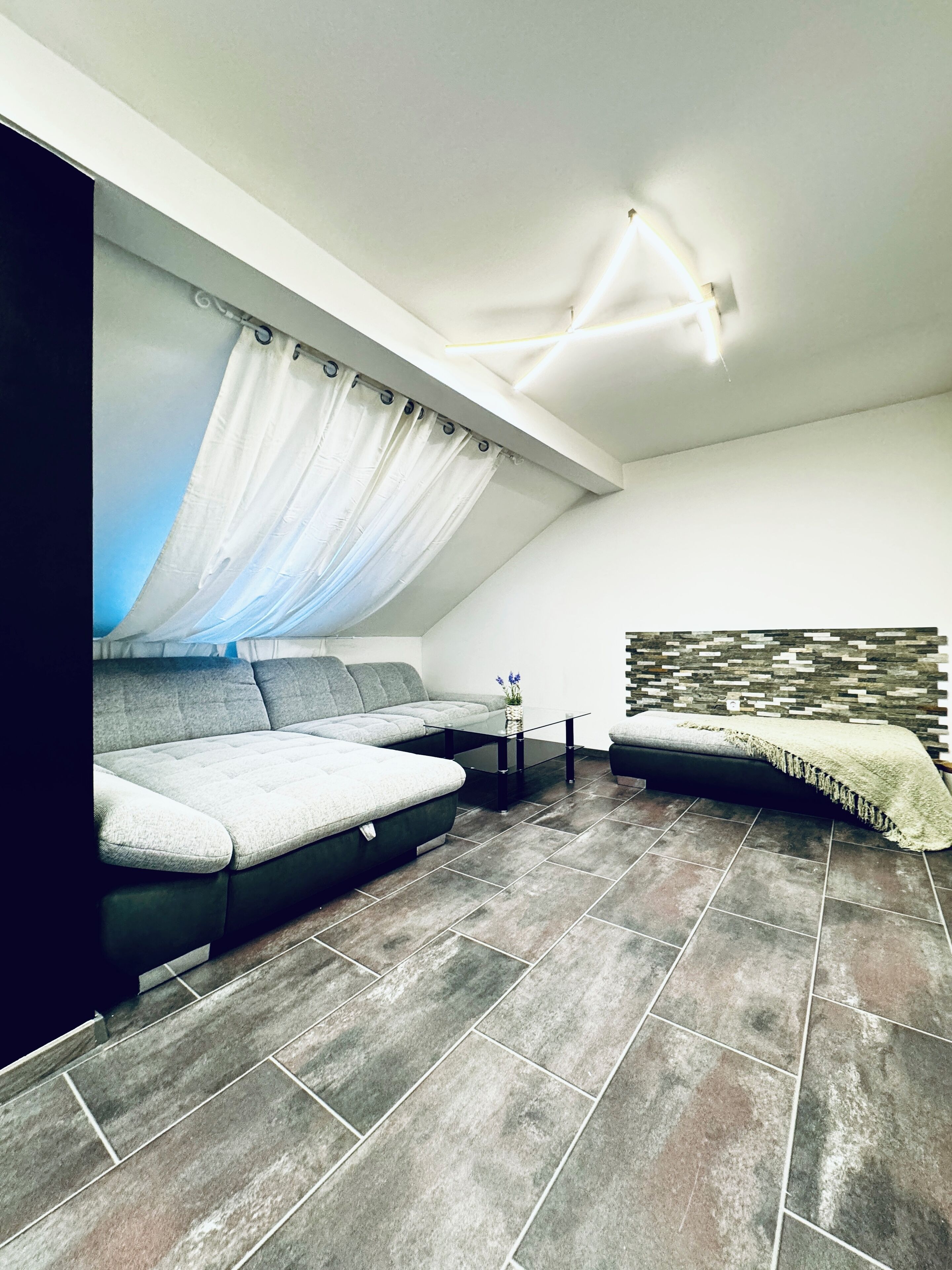 A modern living room with a sectional sofa, a glass coffee table, and a patterned wall.