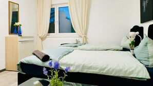 Une chambre moderne avec une table basse en verre, un lit avec une literie blanche, une fenêtre avec des rideaux et une petite plante sur la table.