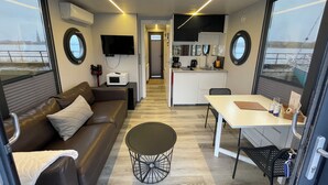 Ein kompakter Wohnbereich mit Sofa, Esstisch, Küchenzeile und großen Fenstern mit Blick hinaus.
