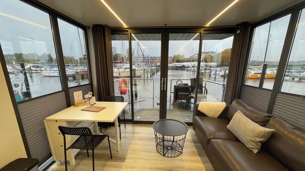 Ein modernes Zimmer mit großem Fenster und Blick auf eine Marina, inklusive einer Couch, einem Tisch und einem Sessel.