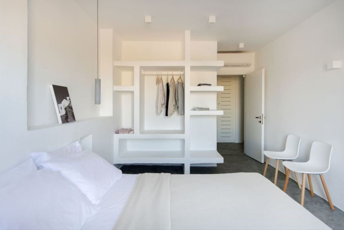 Quarto moderno com uma cama grande, guarda-roupa embutido e área de estar com duas cadeiras.