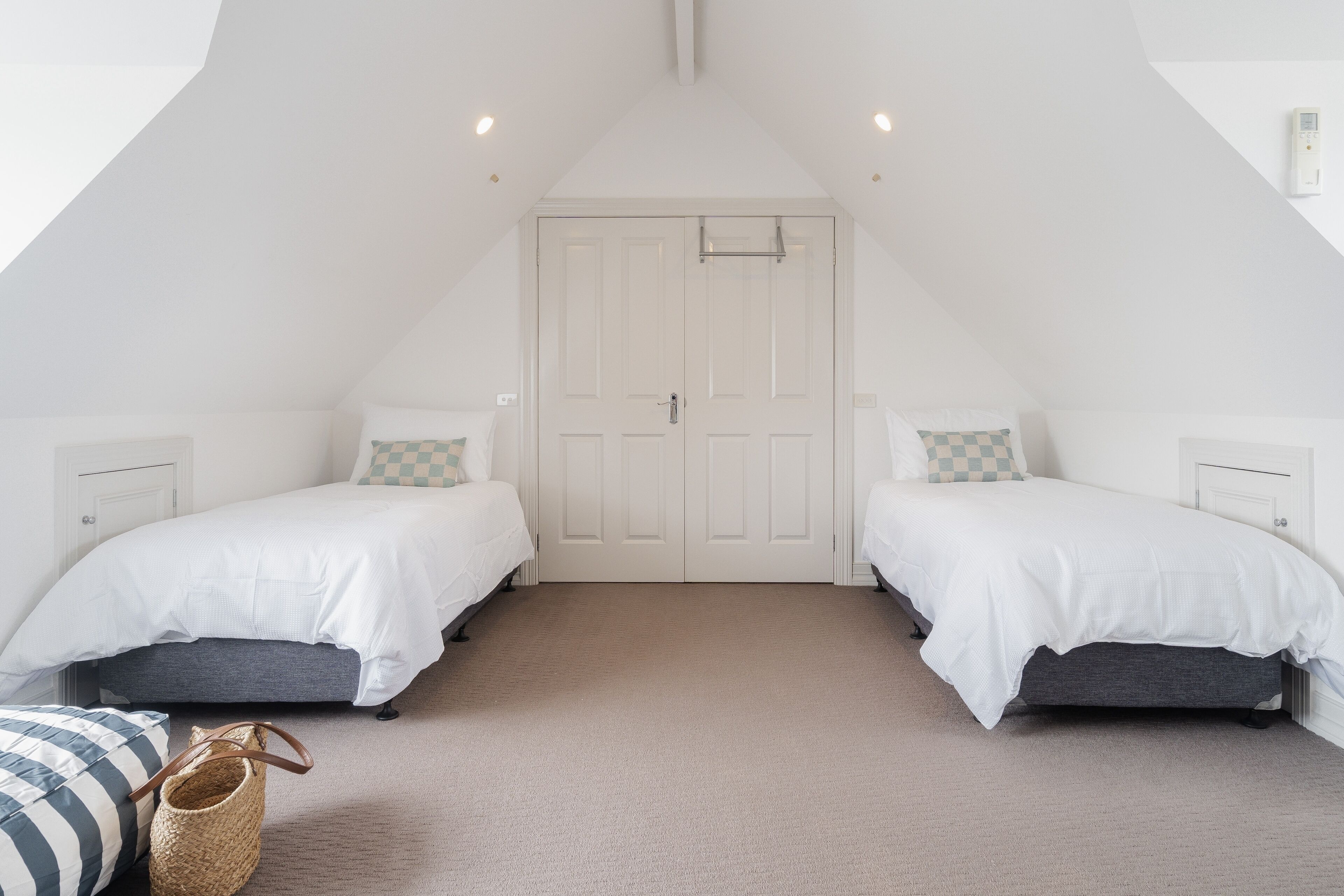 A bedroom with two beds, a large white door, and a sloped ceiling.