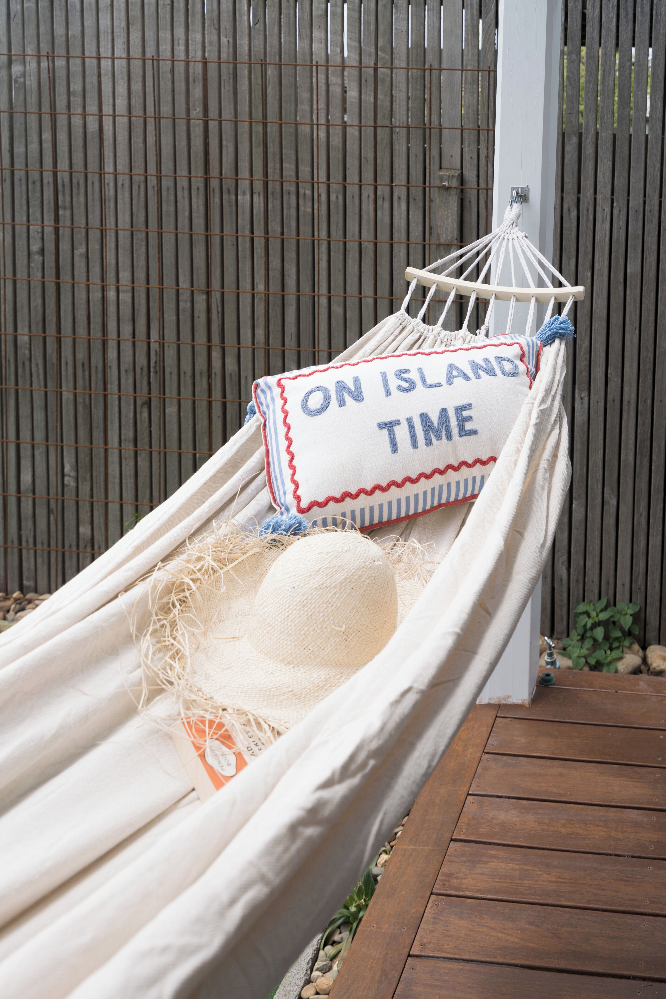 Un hamac avec un coussin sur lequel est inscrit « TEMPS D’ÎLE » et un chapeau de paille.