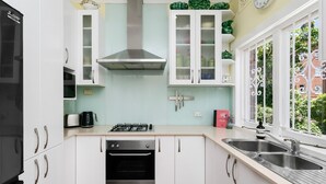 A modern kitchen with white cabinets, a stainless steel range hood, a built-in oven, a double sink, and a window with a view of greenery. - Mosman Bay - ROSE2 - Rose Crescent - Art Deco Mosman Bay home (Mosman)