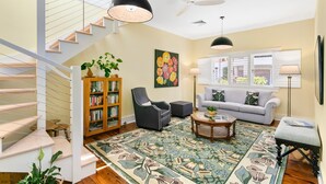 A modern living room with a staircase, a sofa, a bookshelf, and a large floral rug. - Mosman Bay - ROSE2 - Rose Crescent - Art Deco Mosman Bay home (Mosman)