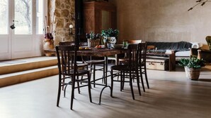 A dining area with a rustic wooden table and chairs, surrounded by stone walls and a large window. - La Pagliera  (Agrigento)