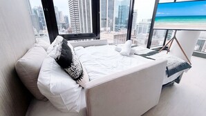 Ein modernes Hotelzimmer mit einem großen Bett, weißer Bettwäsche und Blick auf die Stadt durch große Fenster.