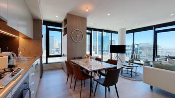 A modern kitchen with a dining area, large windows, and a city view.