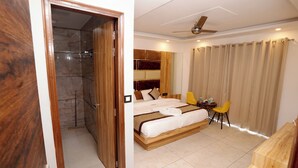 A hotel room with a wooden bed, a small table with chairs, a shower area, and a ceiling fan. - Hotel Silver Inn by PENTAURA (Rishikesh)
