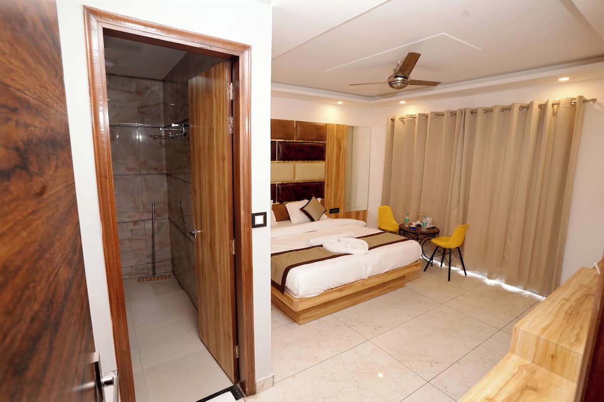 A hotel room with a wooden bed, a small table with chairs, a shower area, and a ceiling fan.
