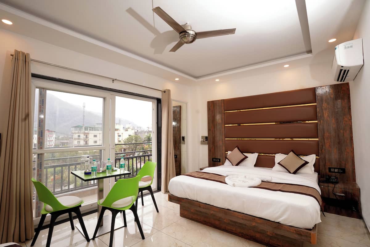 A modern hotel room with a large bed, a ceiling fan, a balcony with a table and chairs, and a view of the city.