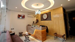 A reception area with a wooden reception desk, a clock, a television, and a bench. - Hotel Silver Inn by PENTAURA (Rishikesh)