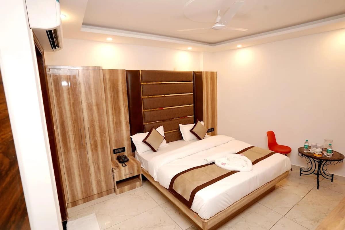 A hotel room with a large bed, a wooden wardrobe, a red chair, and a small table with water bottles.