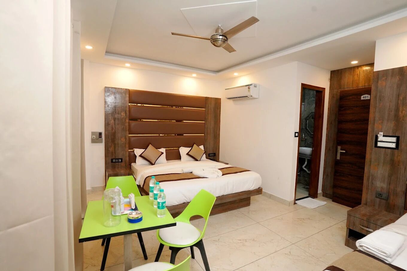 Una habitación de hotel con cama, escritorio y sillas, ventilador de techo y aire acondicionado.