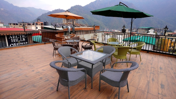 A rooftop terrace with wicker furniture, a glass table, and two umbrellas. - Hotel Silver Inn by PENTAURA (Rishikesh)