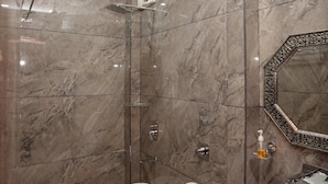 A modern bathroom with a marble wall, a white toilet, a black sink, a shower with a glass door, and a ceiling fan. - Hotel Silver Inn by PENTAURA (Rishikesh)
