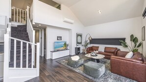 A spacious living area with a staircase, a flat-screen TV, leather sofas, and a coffee table. - Fun for Families: Location, Cinema, Games, Wifi (Perth)