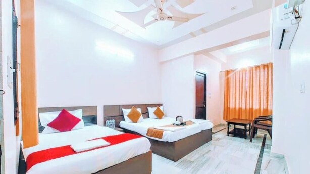 A hotel room with two beds, a ceiling fan, a small table, and a window with curtains. - Hotel shri ram krishna mahal (Ayodhya)