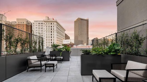 A rooftop terrace with outdoor seating, a city skyline view, and a modern building in the background.