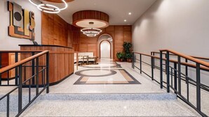 A modern hotel lobby with a reception desk, wooden paneling, a marble floor, and a staircase.