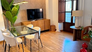 Una sala moderna con una mesa de comedor de vidrio, un televisor y una planta grande.