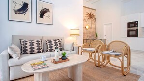 Ein modernes Wohnzimmer mit einer Couch, einem Couchtisch und Korbstühlen. Auf dem Tisch liegt eine Zeitschrift, es gibt eine Lampe und ein Bild an der Wand.