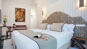 Ein ordentlich eingerichtetes Hotelzimmer mit einem großen Bett, einem Nachttisch mit Lampe, einem Sessel und einer Wandleuchte.