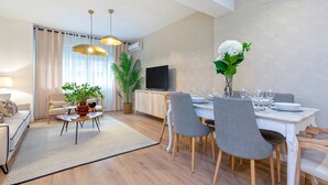 A modern living room with a dining area, featuring a sofa, a coffee table, a TV, and a dining table set for six. - Exclusive apt 3rooms in Granada Martinez Campos II (Granada)