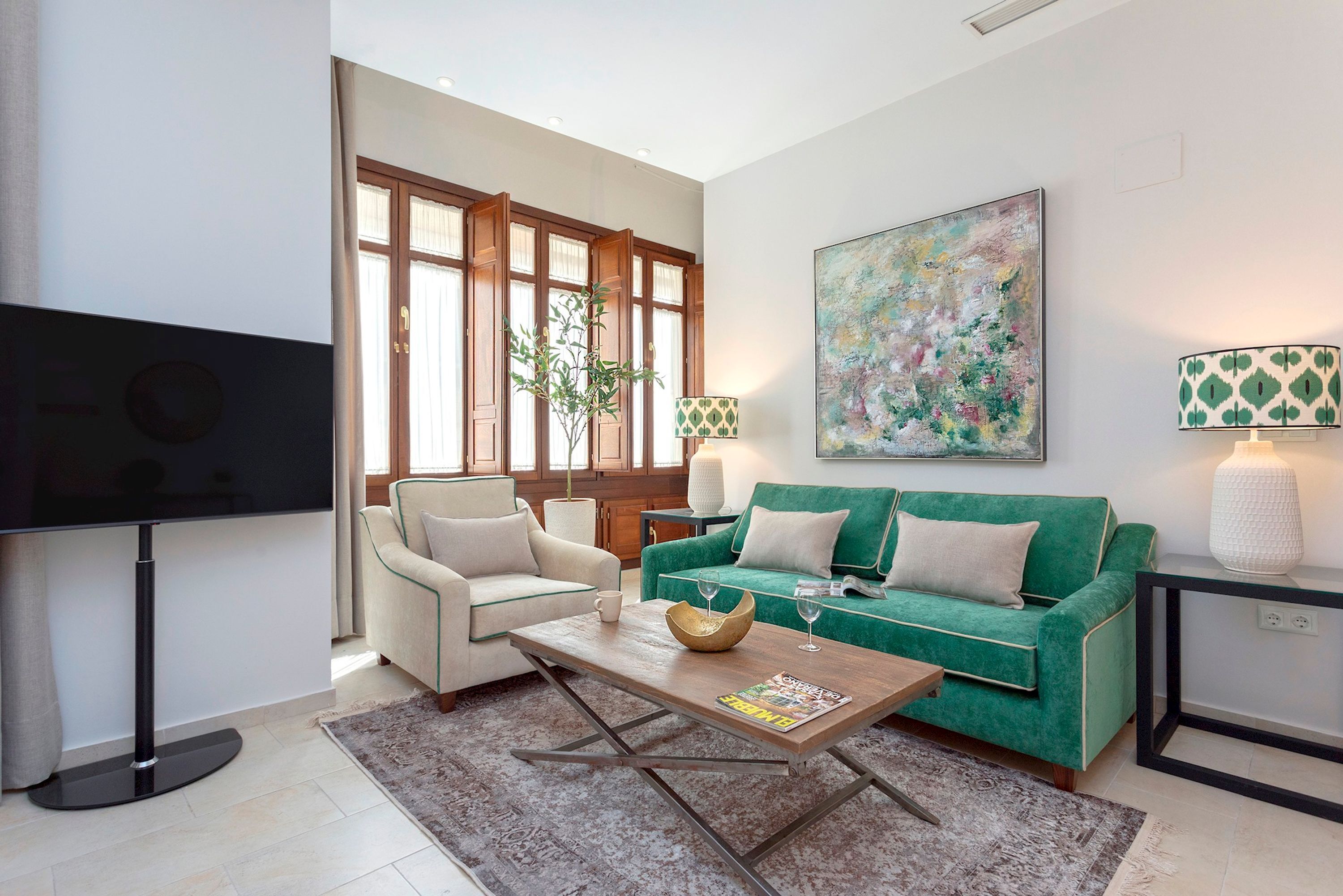 A modern living room with a flat-screen TV, a green sofa, a white armchair, and a coffee table.