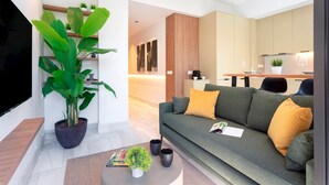 Ein modernes Wohnzimmer mit einem großen Flachbildfernseher, einem grünen Sofa mit gelben Kissen, einem Couchtisch mit einer Pflanze und einem Blumentopf.