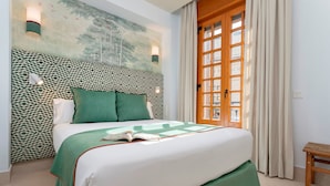 A neatly made bed with a green bedspread and pillows, a patterned headboard, and a window with curtains. - Bright Apartment in the Heart of Seville Tom s de Ibarra II (Seville)