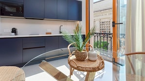 A modern kitchen with dark cabinets, a microwave, and a coffee machine. There's a glass table with a woven basket and a white vase. A balcony with a wrought iron railing and a view of a building with columns is visible. - Bright Apartment in the Heart of Seville Tom s de Ibarra II (Seville)